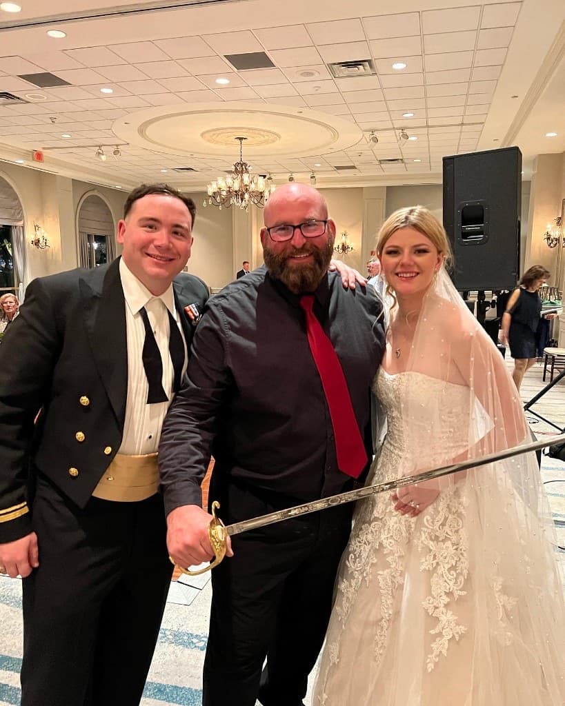 Gary Lucca with a bride and a naval officer groom holding a ceremonial sword after their wedding reception